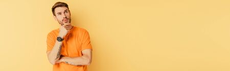 panoramic shot of pensive young man touching chin and looking up isolated on yellowの写真素材