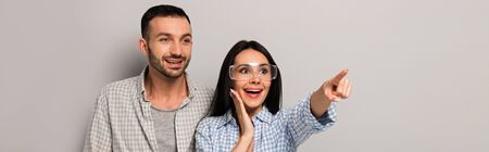 panoramic shot of excited manual workers in goggles with tool belt pointing on greyの写真素材