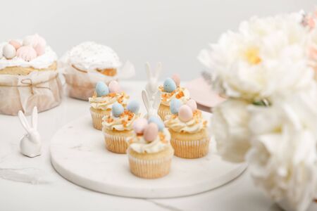 Selective focus of cupcakes with decorative bunnies on round board, flowers and easter cakes...