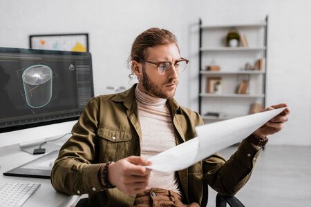 3d artist looking at blueprint while working on project of 3d design in office