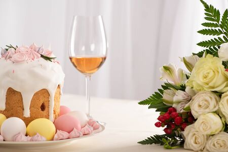 delicious Easter cake decorated with meringue with pink and white eggs on plate near flowers and wineの写真素材