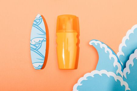 Top view of dispenser bottle of sunscreen with paper cut sea waves and surfboard on orange...