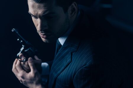 Gangster with revolver in clenched hands on dark background