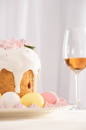 selective focus of Easter cake decorated with meringue near colorful eggs on plate and wine glassの写真素材