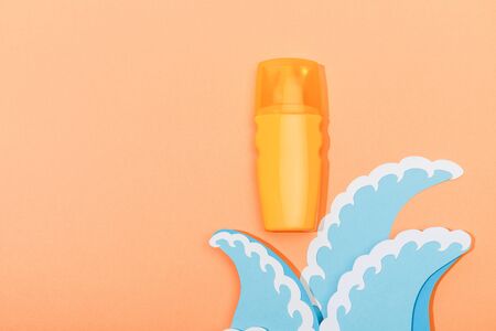 Top view of dispenser bottle of sunscreen with paper cut sea waves on orange backgroundの写真素材