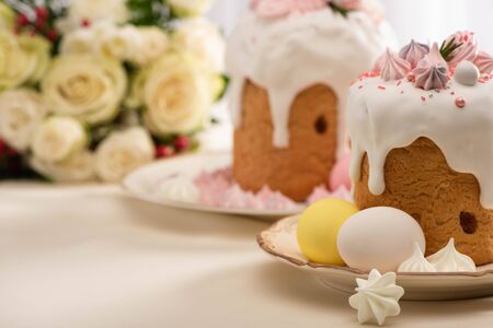 selective focus of delicious Easter cakes decorated with meringue near eggs on plate and flowersの写真素材
