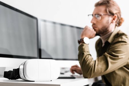 Selective focus of vr headset on table near 3d artist looking at computer monitor on table isolated on greyの写真素材