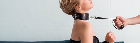 panoramic shot of man in holding bdsm leash on submissive womanの写真素材