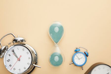 top view of classic alarm clocks and hourglass on beige background