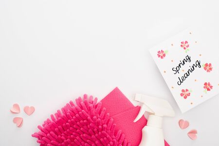 top view of pink cleaning supplies and hearts near spring cleaning card on white background