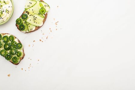 top view of fresh cucumber toasts with seeds, basil leaves near yogurt in bowl on white background