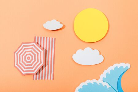 Top view of paper cut summer beach with umbrella and blanket on orange backgroundの写真素材