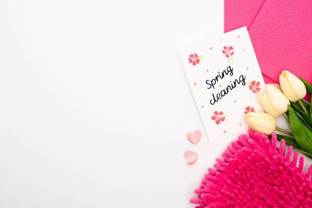 top view of tulips and pink cleaning supplies near spring cleaning card on white background