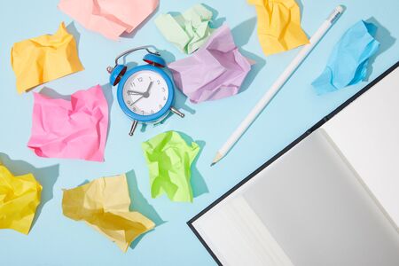 top view of classic alarm clock with blank netbook and pencil on blue background with crumpled...