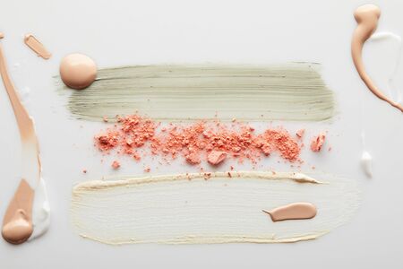 Top view of cosmetic and tone cream, clay brushstrokes with pink blusher on grey background