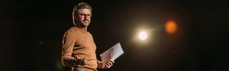 panoramic shot of mature actor holding scenario and standing on stage during rehearse in theater