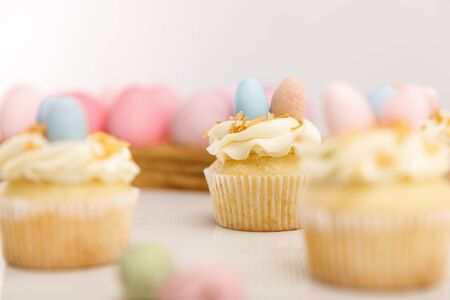 Selective focus of delicious cupcakes with easter eggs on wooden board on grey background
