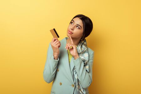 pensive african american girl holding credit card and pointing with finger on yellowの写真素材