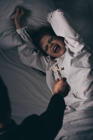 exorcist holding cross over creepy screaming demon in bedの写真素材