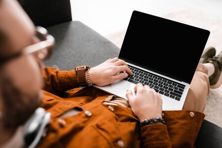 Selective focus of 3d artist working on laptop with blank screen on couch