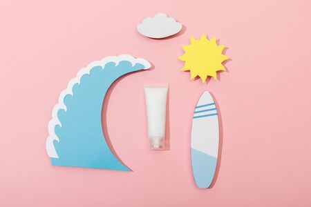 Top view of paper cut sun, cloud, sea wave and surfboard with tube of sunscreen on pink backgroundの写真素材