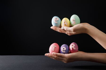 Cropped view of woman holding painted chicken eggs with easter lettering on black and grey