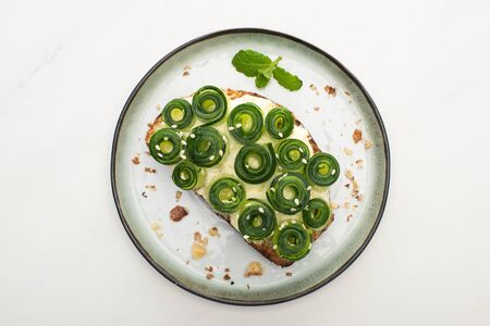 top view of fresh cucumber toast with sesame and mint leaves on plate on white backgroundの写真素材