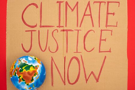 Top view of globe and placard with climate justice now lettering on red background, global warming...