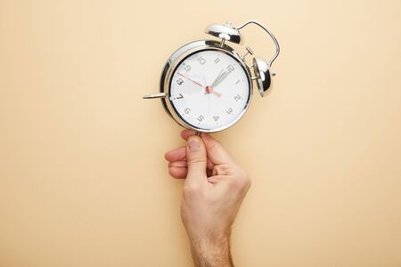 cropped view of man touching classic alarm clock on beige background