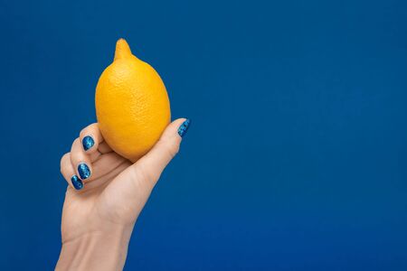 cropped view of woman holding whole lemon isolated on blueの写真素材