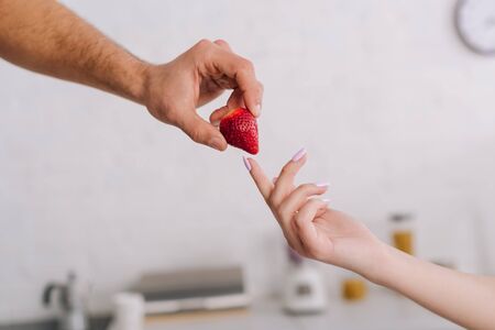 cropped view of man giving strawberry to womanの写真素材