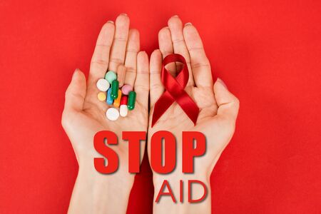 top view of woman holding red ribbon and pills near stop aid lettering on redの写真素材