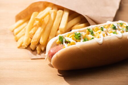 selective focus of delicious hot dog with corn, green onion and mayonnaise near french fries on wooden tableの写真素材