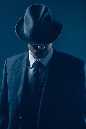 Mafioso with covered eyes with felt hat on dark blue backgroundの写真素材