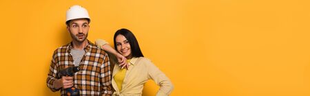 panoramic shot of smiling manual workers holding electric drill on yellowの写真素材