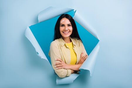 confident workwoman with crossed arms and dirty face in paint standing in torn paper, isolated on...