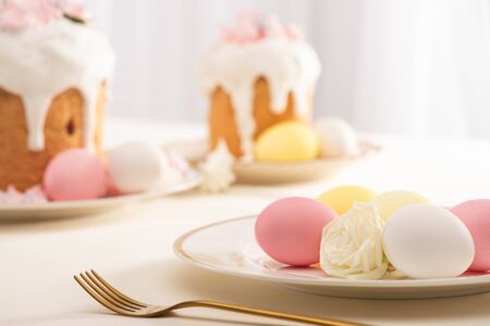 selective focus of delicious Easter cakes with meringue near colorful eggs on plate and fork