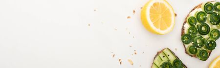 top view of fresh cucumber toasts with seeds near lemon on white background, panoramic shotの写真素材