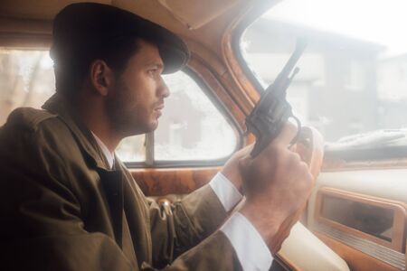 Profile of mafioso in flat cap and coat with gun driving carの写真素材