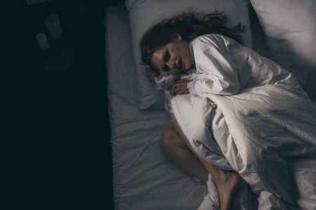 top view of demonic obsessed woman in nightgown lying in bedの写真素材