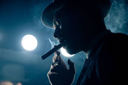 Low angle view of mafioso smoking cigar on dark blue backgroundの写真素材