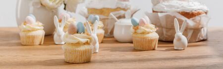 Selective focus of cupcakes with decorative bunnies, sugar bowl, easter cakes and vase on wooden...