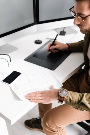 Handsome digital designer using blueprint while working with graphics tablet and computers near vr...