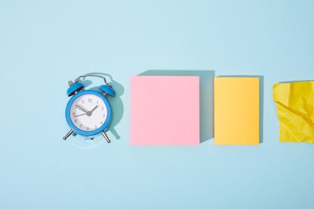 top view of classic alarm clock with colorful sticky notes on blue background
