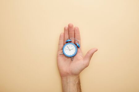 cropped view of man holding small alarm clock on beige background