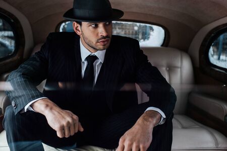 Selective focus of tense mafioso in black suit and felt hat in retro carの写真素材