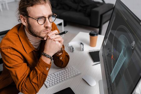 High angle view of thoughtful digital designer holding stylus near project of 3d design on computer...