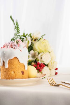 selective focus of delicious Easter cake decorated with meringue with pink and white eggs on plate near flowers and cutleryの写真素材