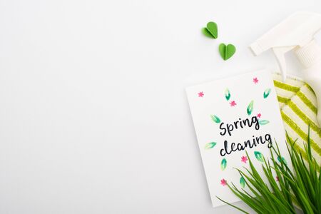 top view of green grass and cleaning supplies near spring cleaning card on white background