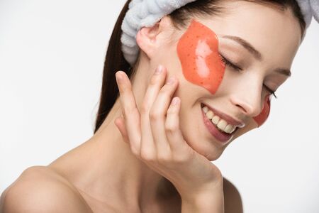 happy girl with closed eyes touching face with lip-shaped collagen patch isolated on white